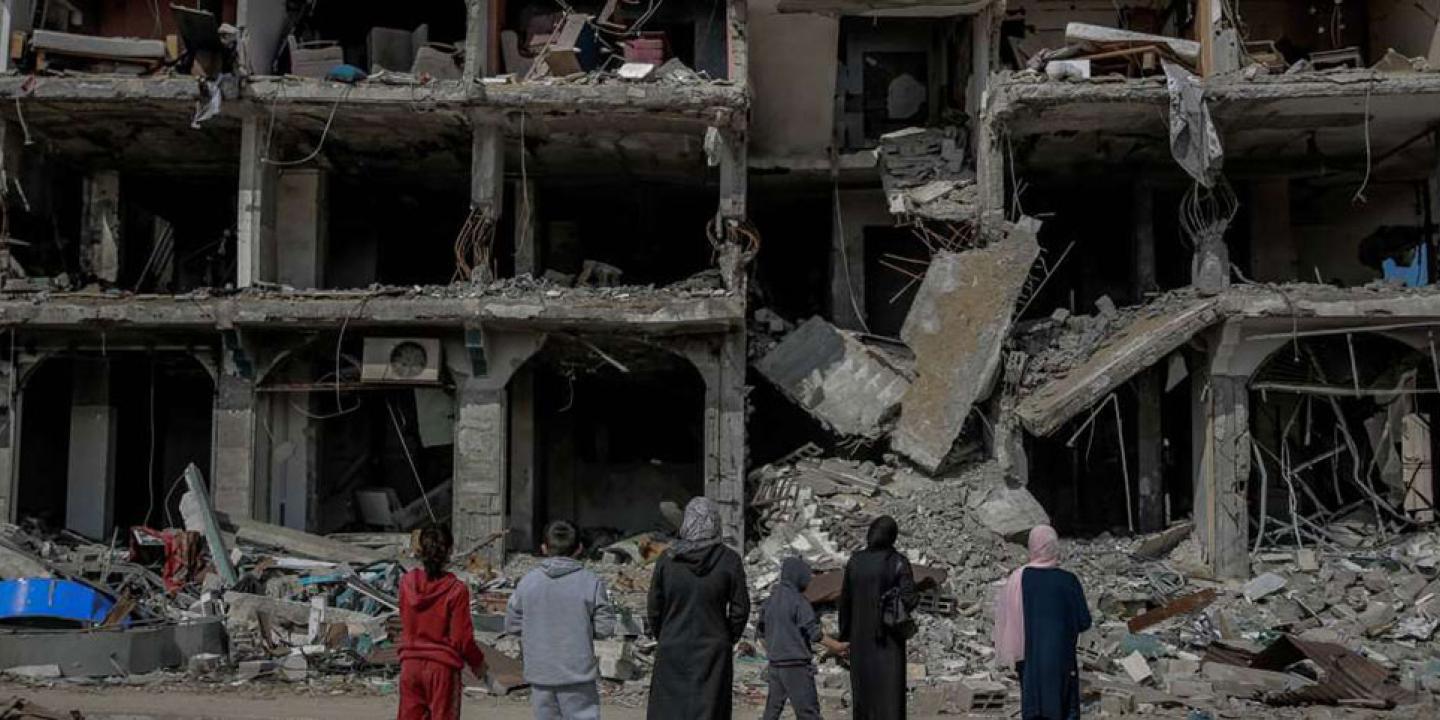 A family look at the concrete shell and remains of a bombed building.