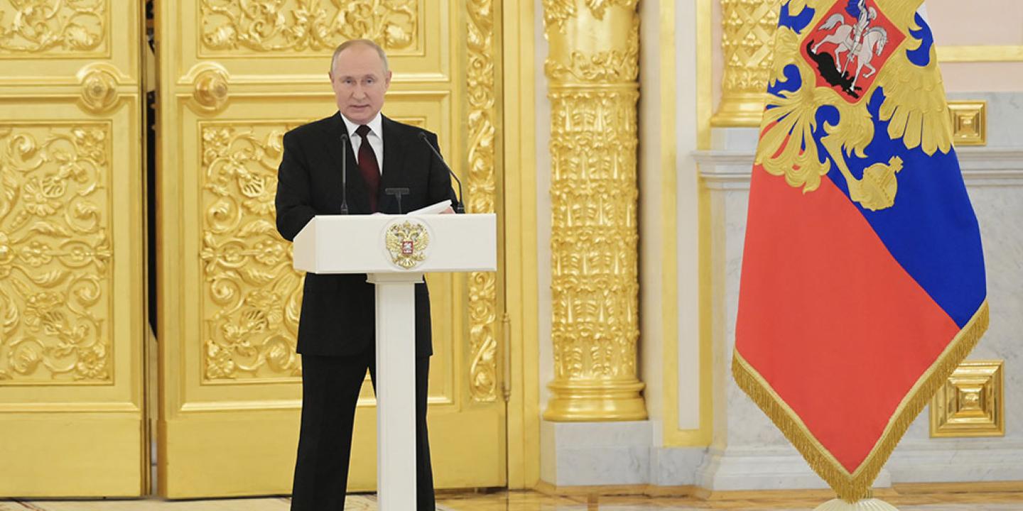 Preisdent Putin stands behind a lectern with a gold door and Russian flag behind him.