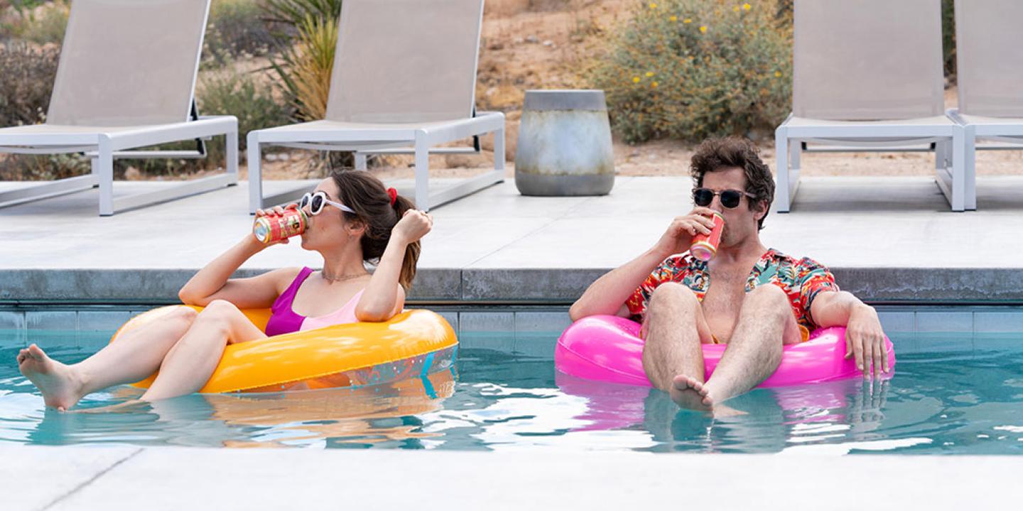 A young couple lounge on floating rings in a swimming pool.