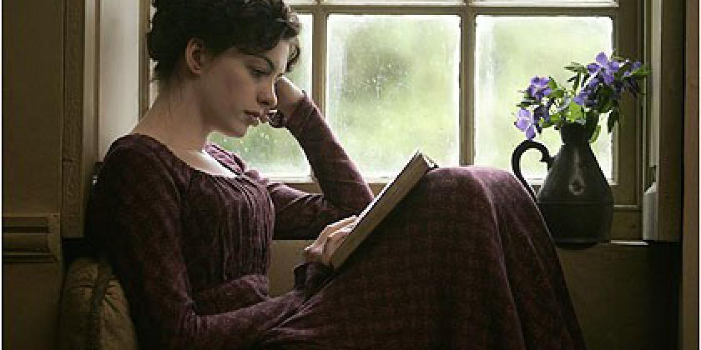 A woman in 18th century clothes sits within a windowsill reading a book