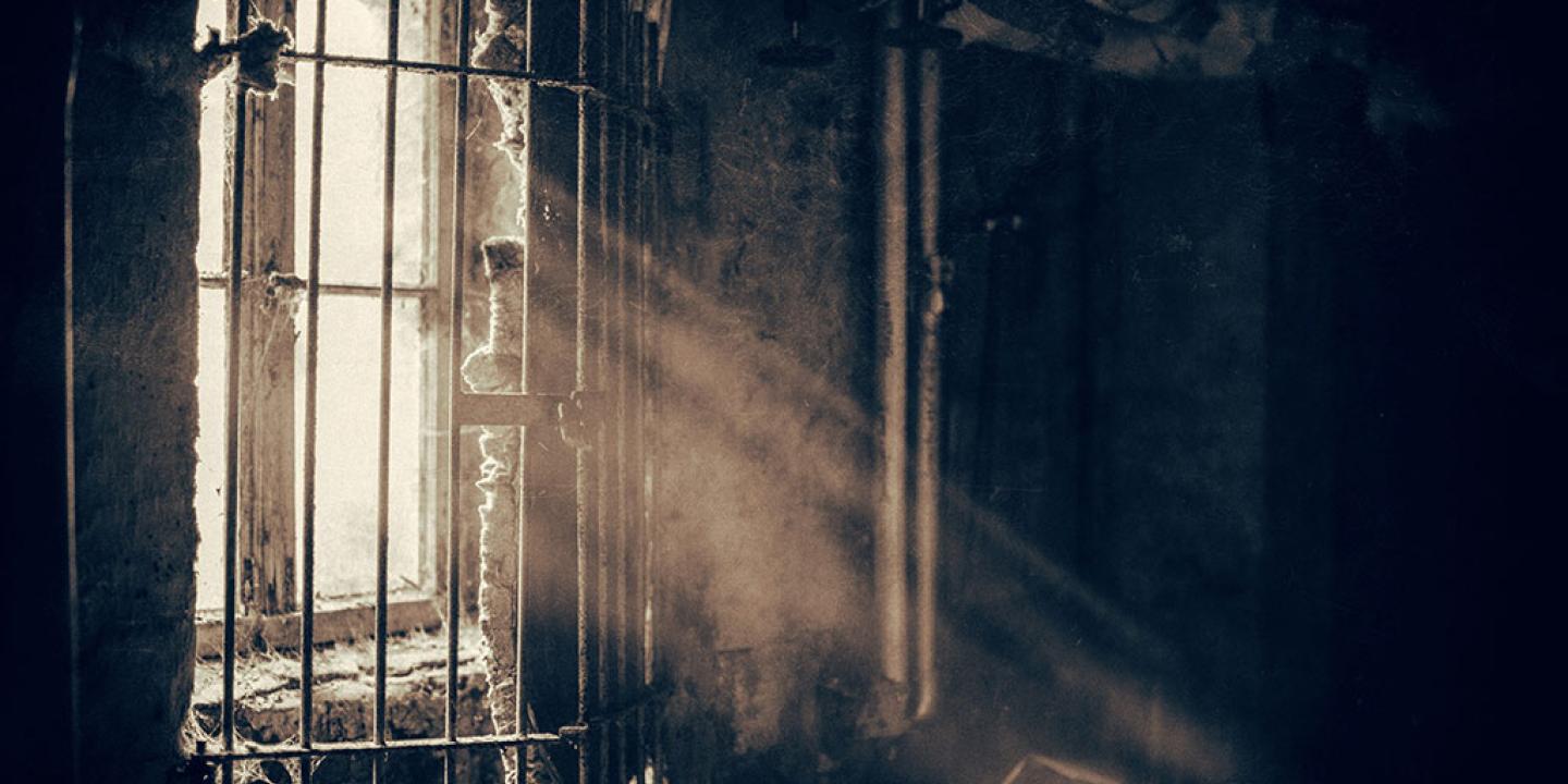 A window sheds light through locked bars into a dusty and dark room,