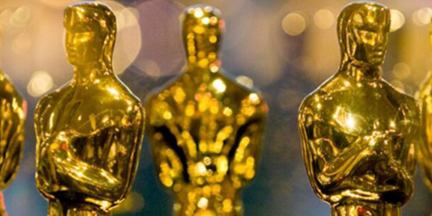 A closely cropped group of gold Oscar statues showing mostly their head and shoulders.