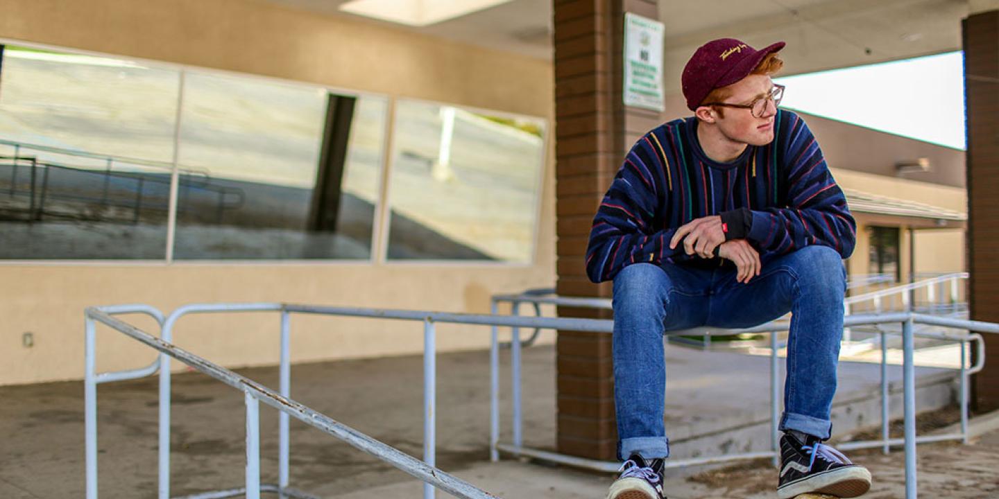 A casually dressed man perches on railing balancing, clasping his hands and looking around.