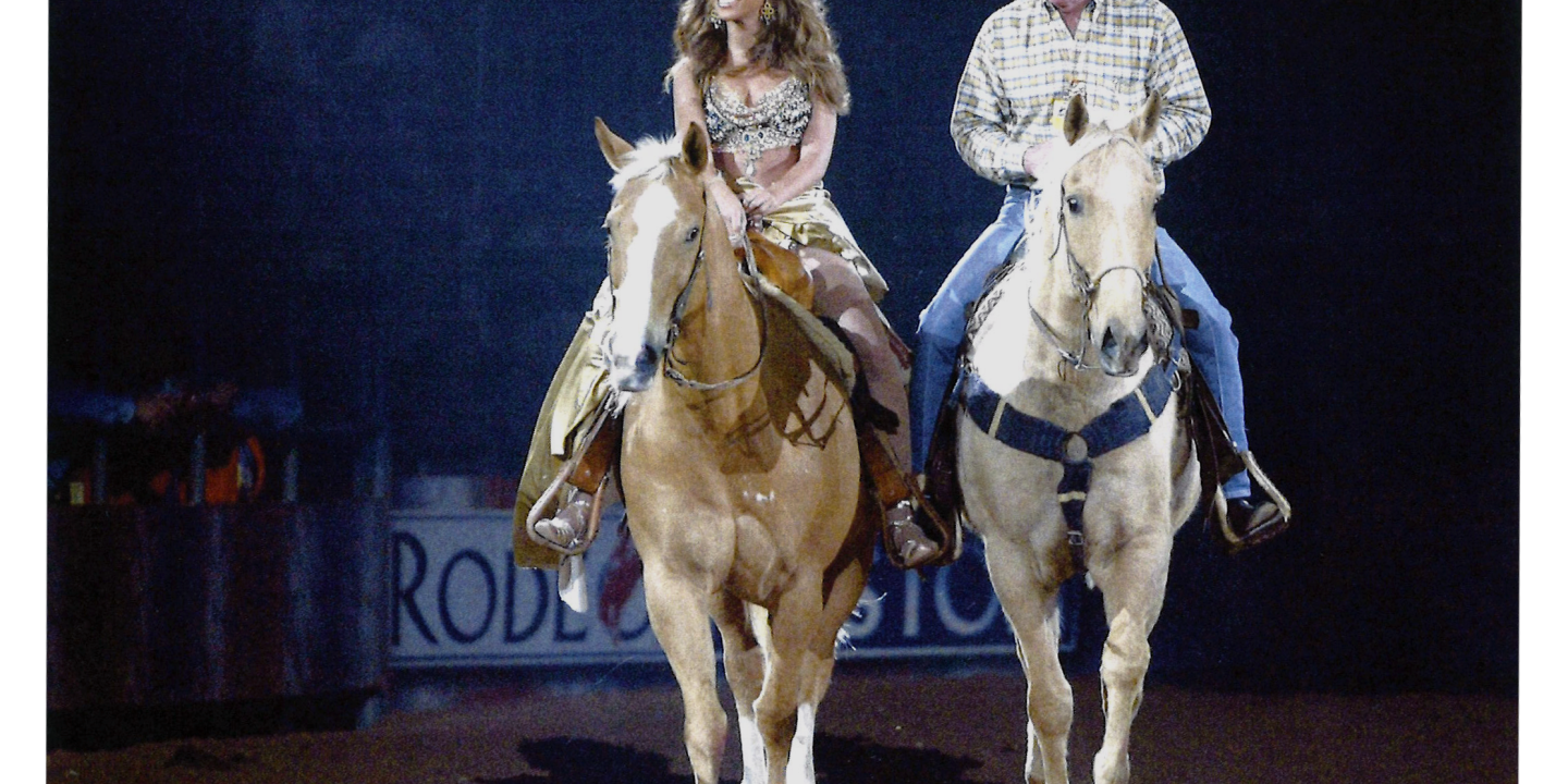 Side by side, two rodeo riders on horses trot toward the camera. One is Beyonce, the other a cowboy