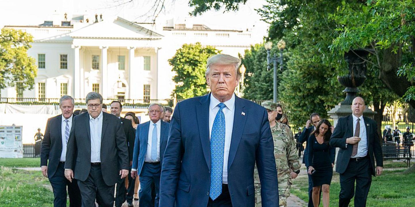 A fierce looking man walks at the head of a phalanx of suited men.