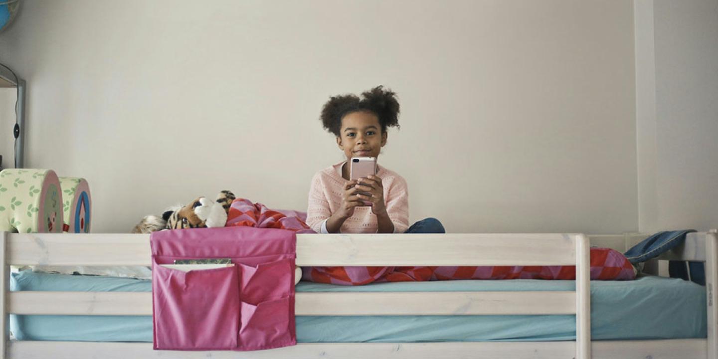 A child sits atop a bunk bed holding a phone in front.