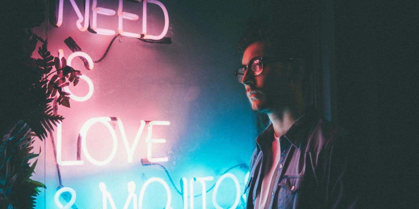 A man stands and looks at a neon sign reading 'need love and... '