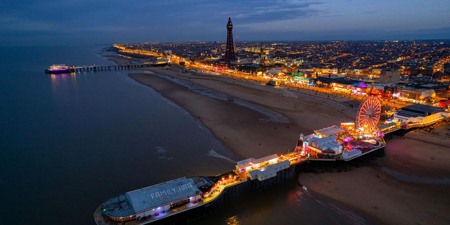 An aerial view at dusk of a brightly lit pier and promenade of the seaside town of Blackpool