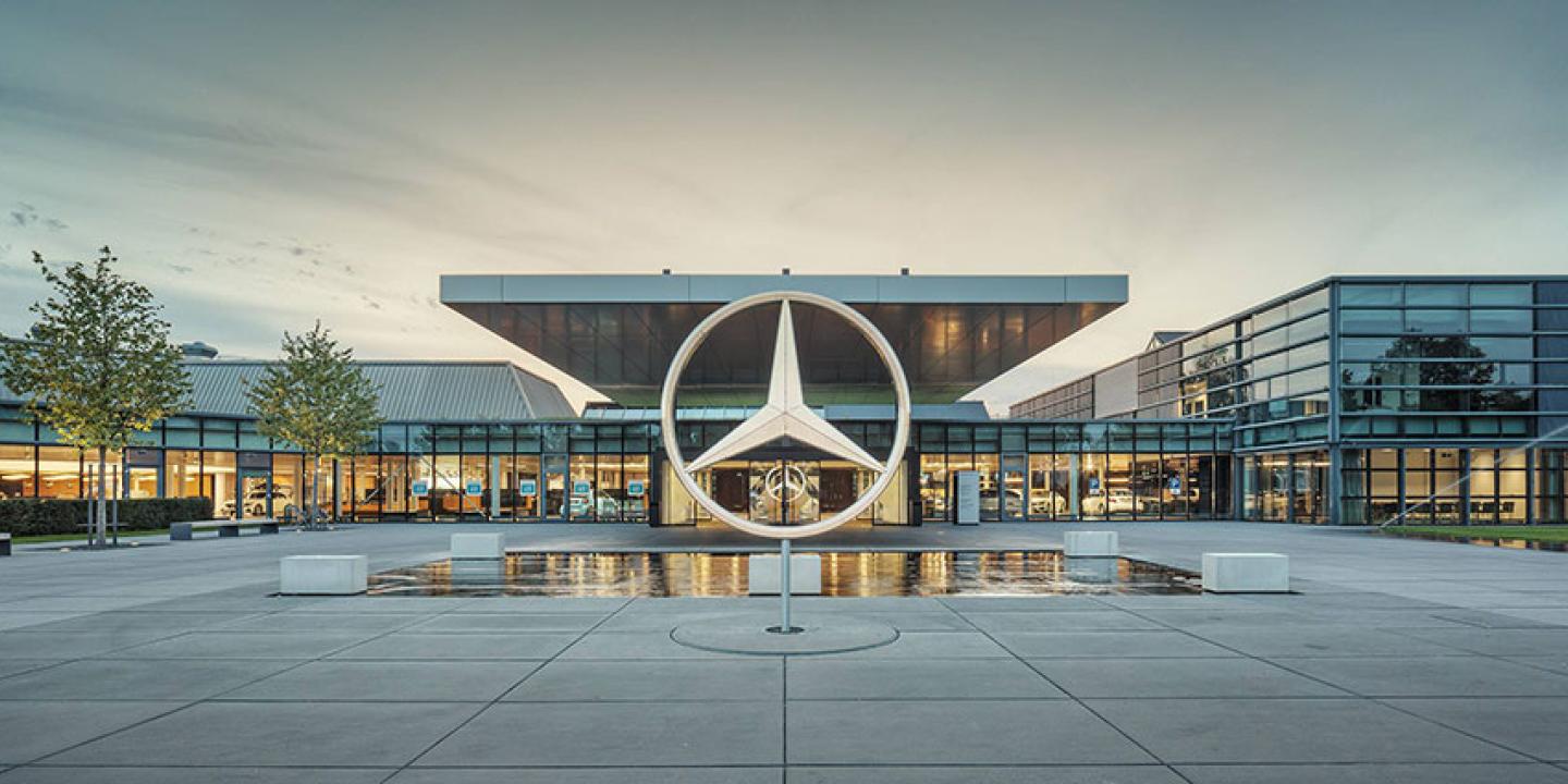 A large sculpture of the Mercedes Benz three-point star stands in front of a large, low glass fronted showroom.