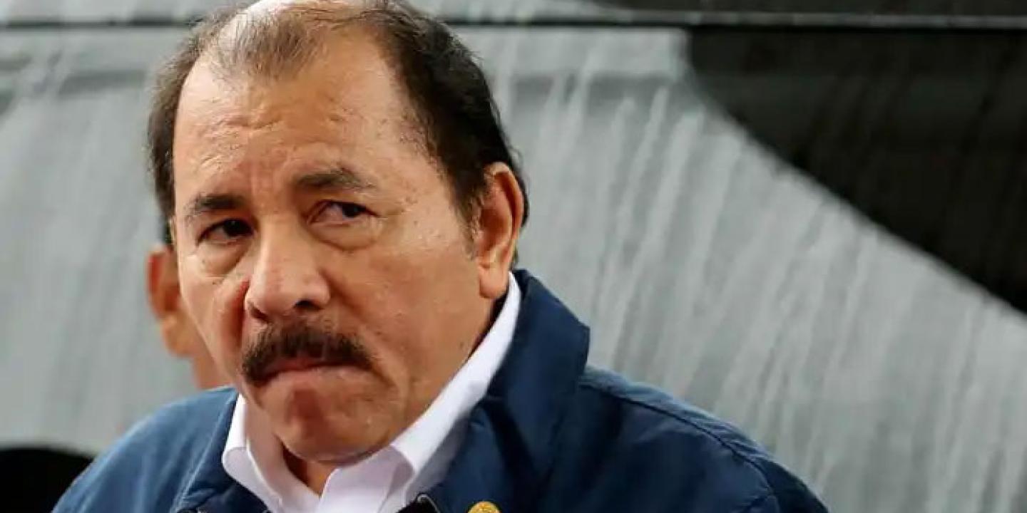 An balding man with a moustache turns to look at a camera. 