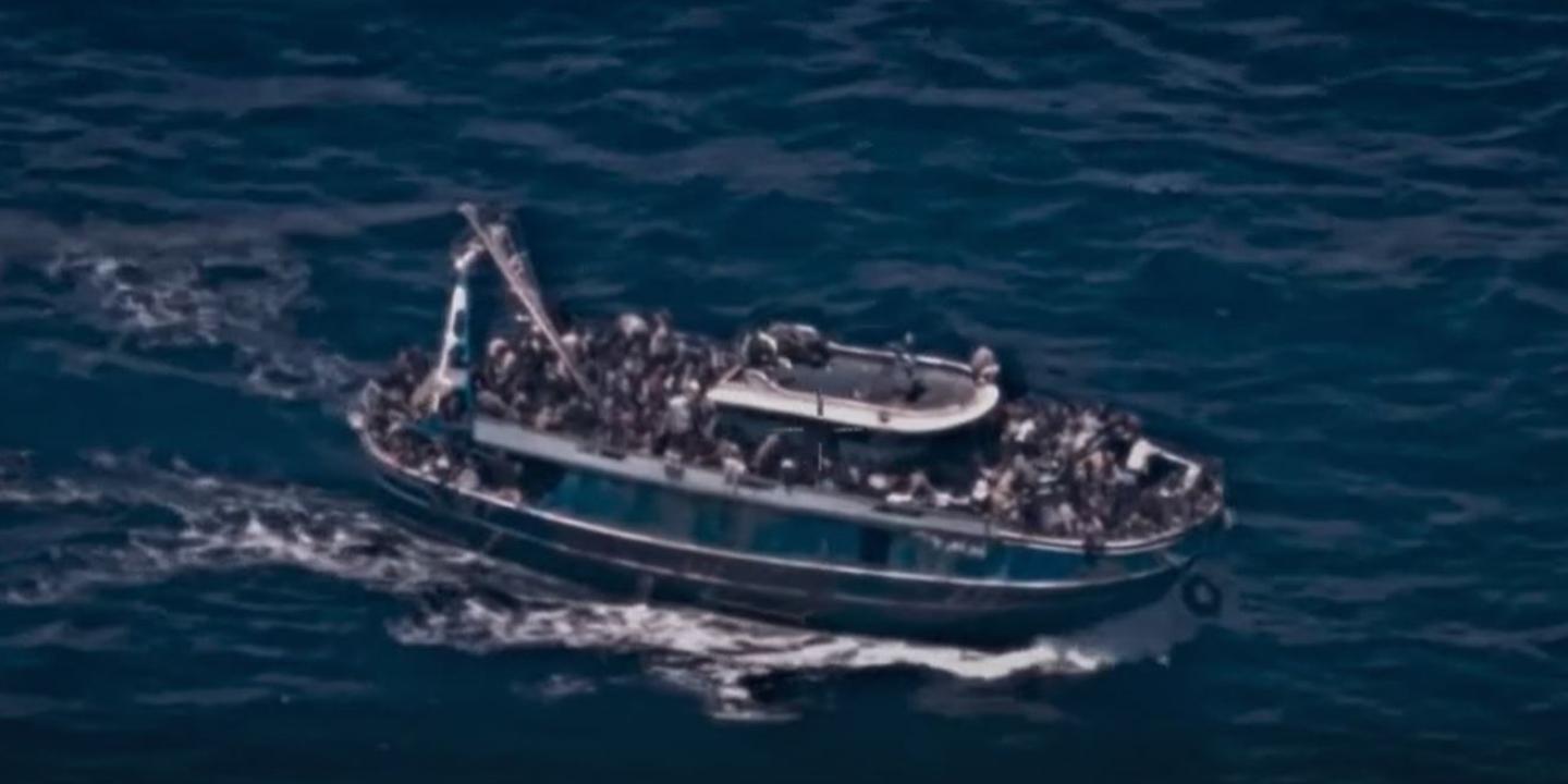 A grainy surveillance picture of an rusty boat overloaded with people