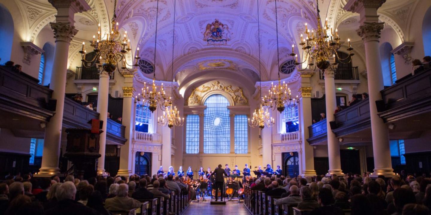 A choir sing at the front of a church while an audience looks on.