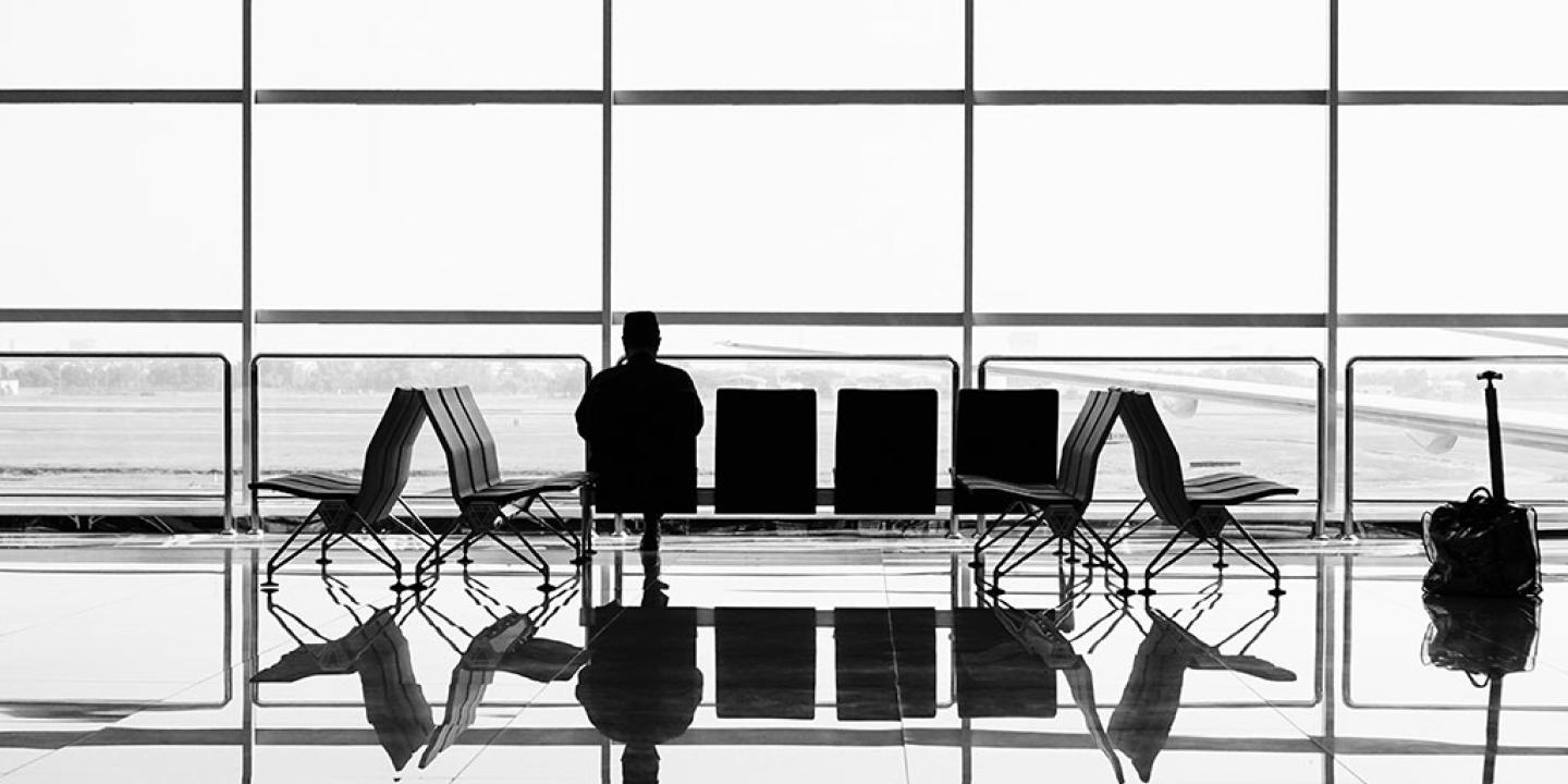 A large airport window silhouettes a bench at which one person sits.