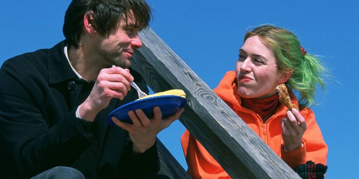 A coupe sit on outdoor steps against a blue sky. One holds a plate and the other looks towards them.