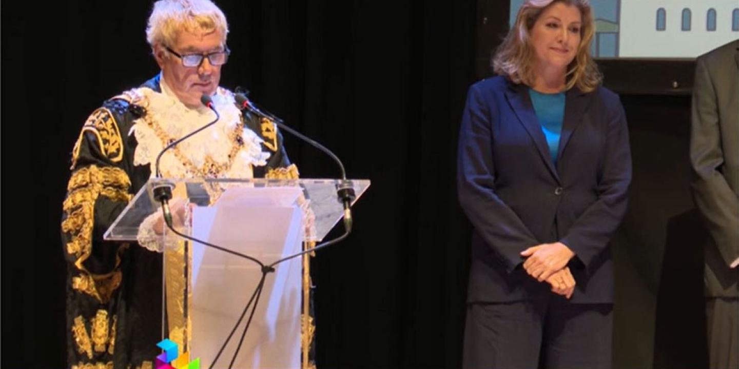 A mayor reads an election result as a despondent candidate looks on.