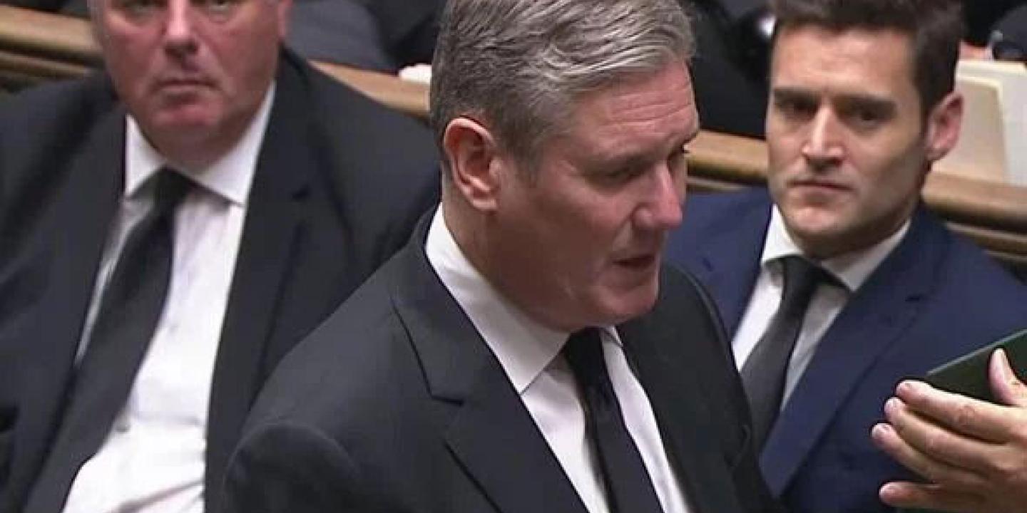 Keir Starmer stands in the House of Commons and recites an oath from a card held up in front of him.