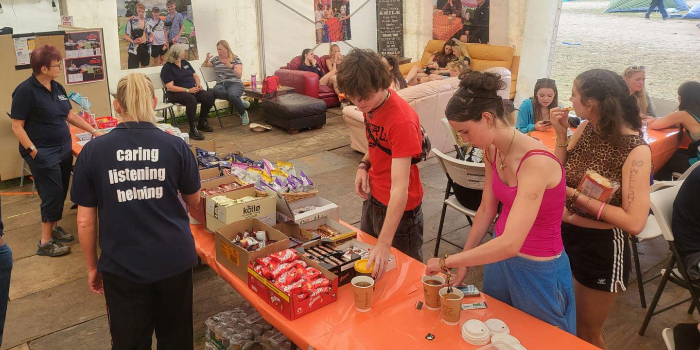 Festival goers, in a cafe tent, make drinks or sit around talking