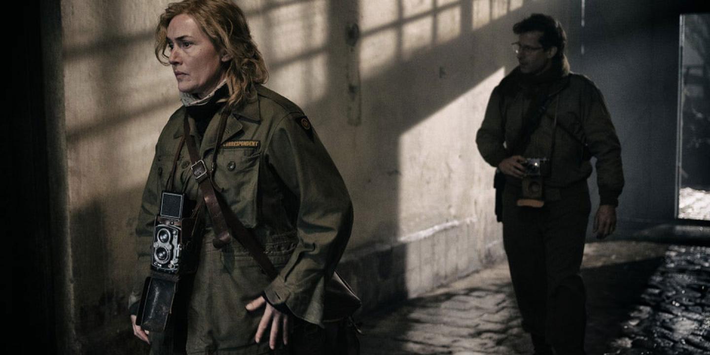 Two war photographers creep along a shadowy corridor.