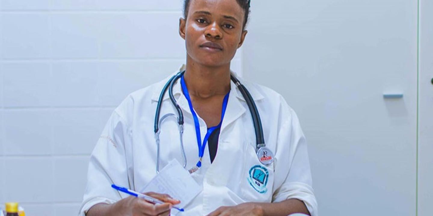 A tired-looking doctor sits at a desk dealing with paperwork.