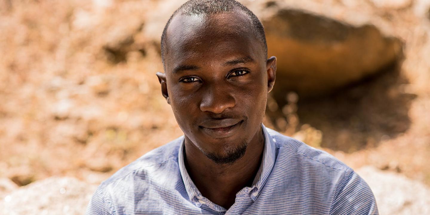 A Nigerian man looks up towards the camera, behind him is dusty ground