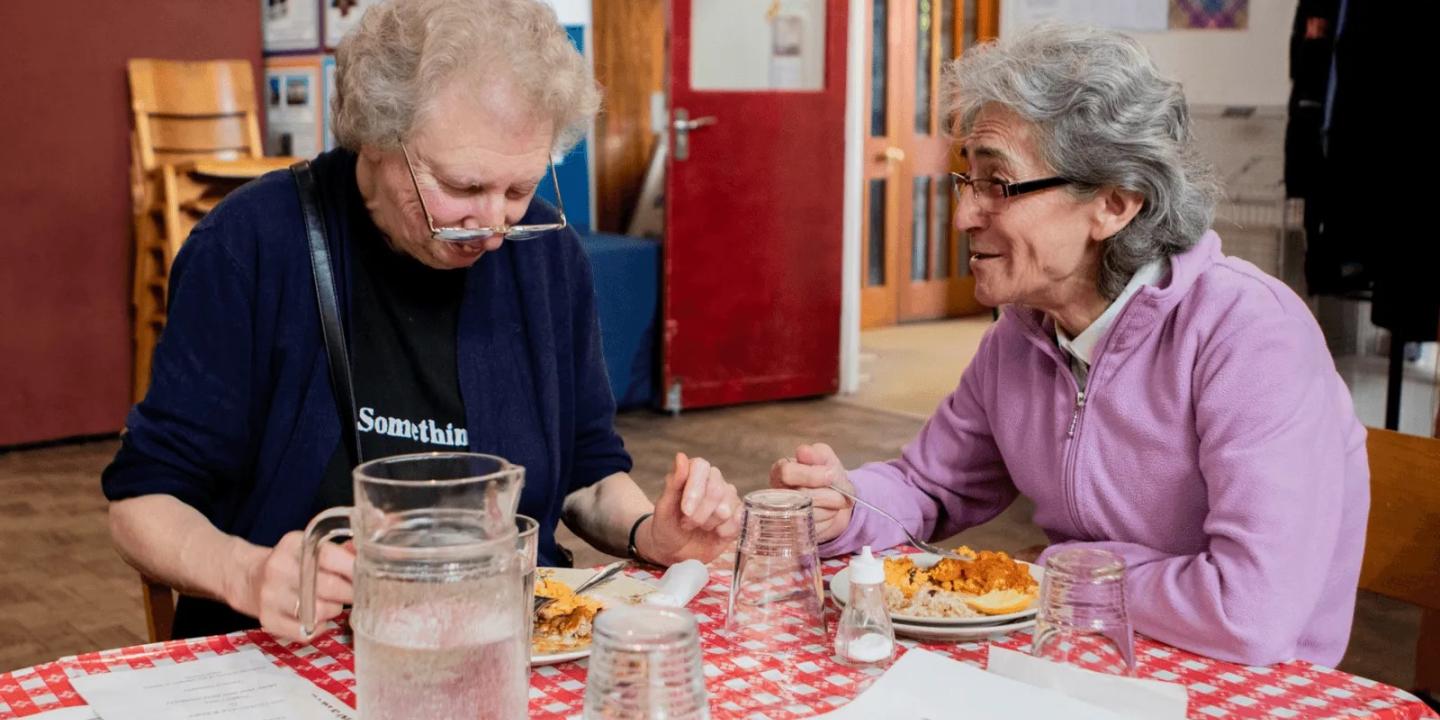 two women sit a table chatting.