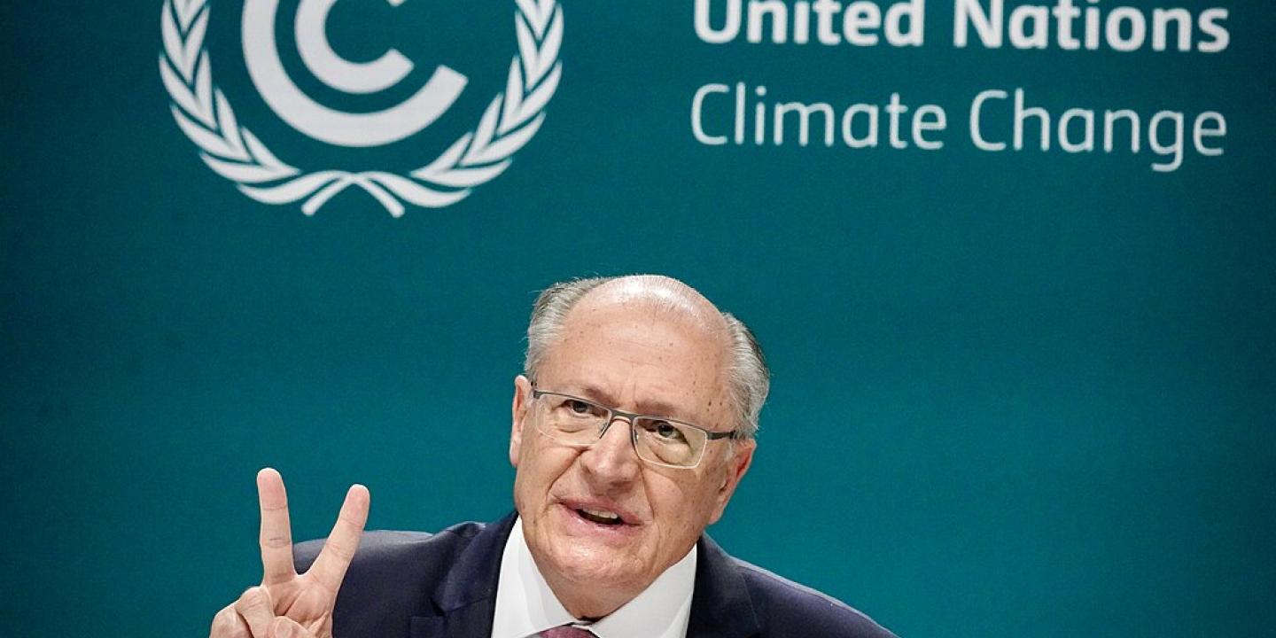 A speaker holds two fingers up while sitting in front of a backdrop reading 'United Nations Climate Change.