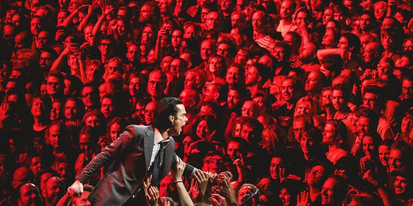 A rock star prowls the stage while behind hundred of faces tined red star.