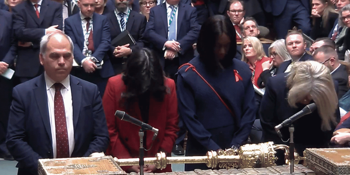 Four MPs stand at a table with heads bowed.