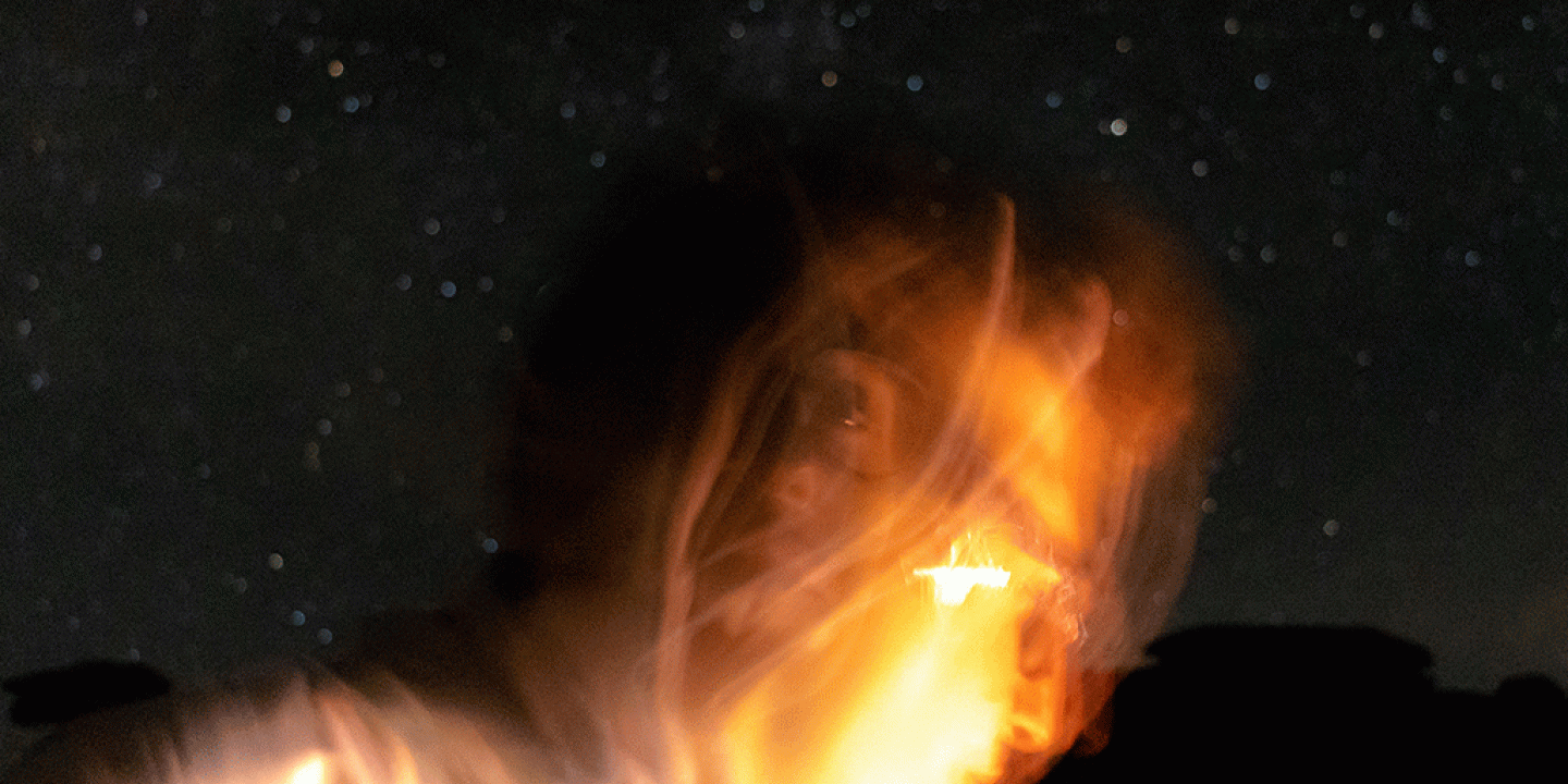 Against a night sky a lit up face is blurred by the camera movement.