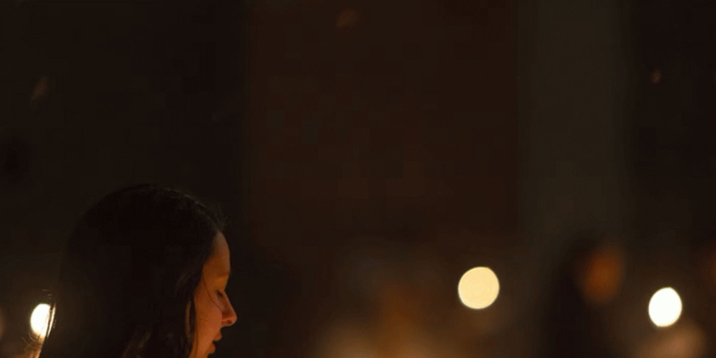 A carol singer looks down while candles flicker.
