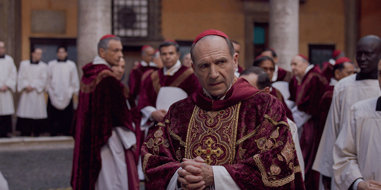A cardinal glances to the side as he stands amid a gather of clergy,