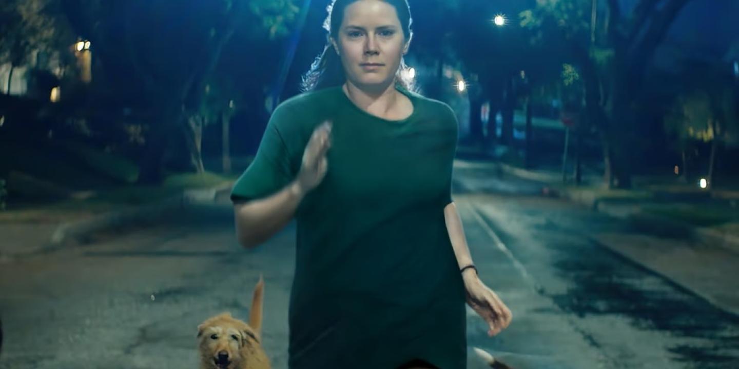 A woman runs down a street at night accompanied by dogs