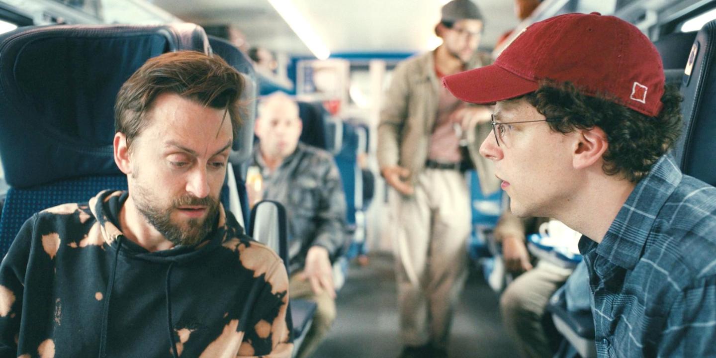 Two male cousins converse across the aisle of a train.