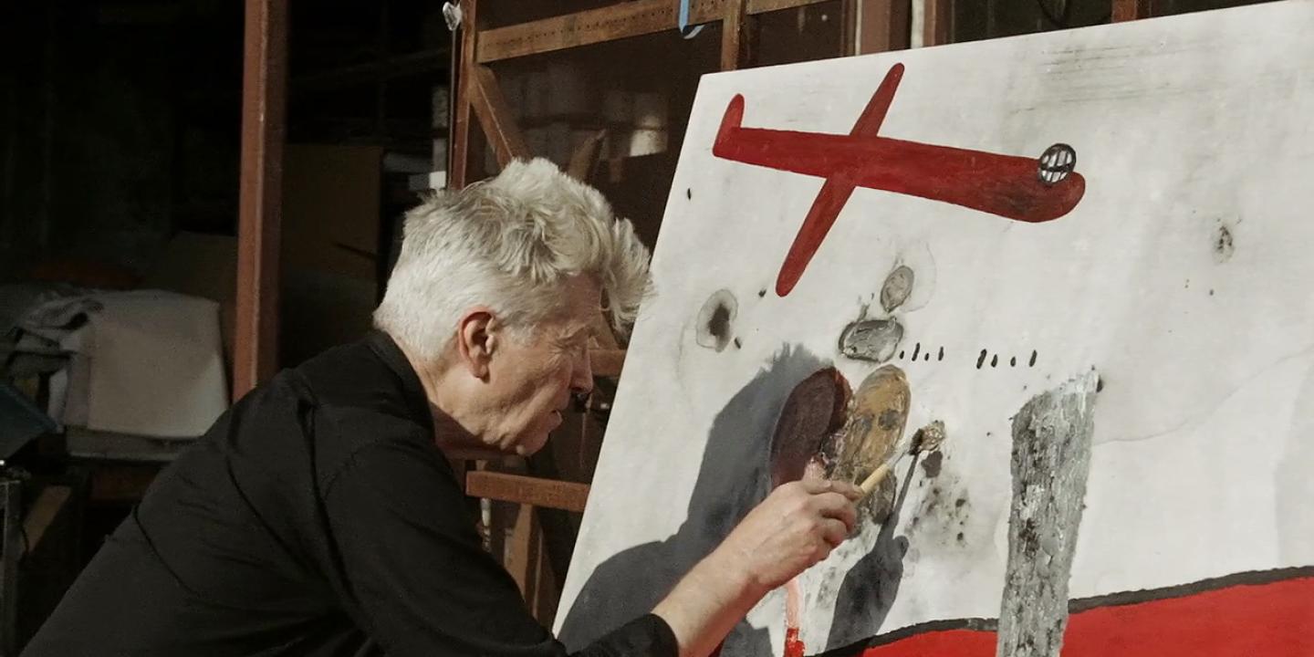 A man paints a canvas with red images.