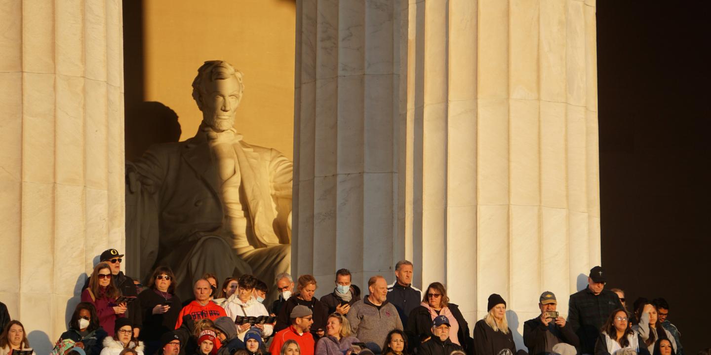 A crowd of people stand in the side steps of the Lincoln Memorial