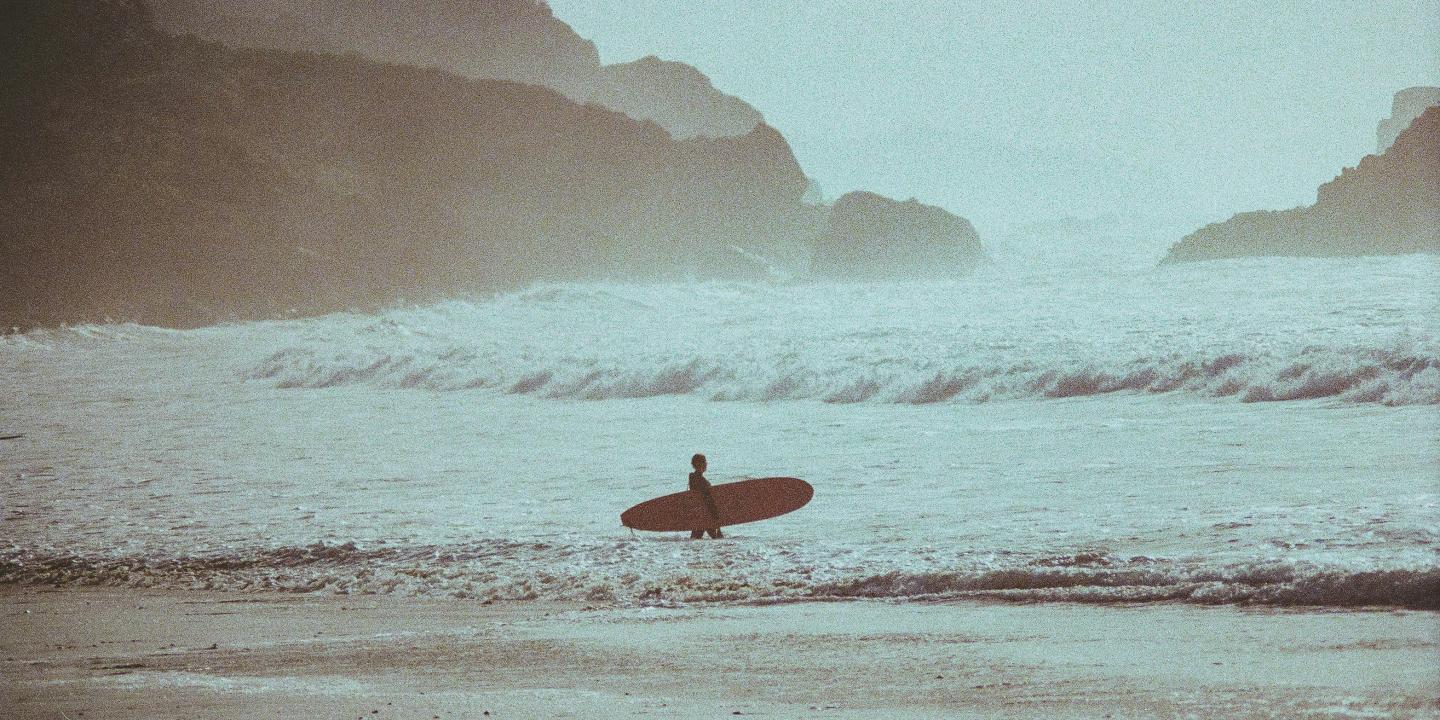 A sufer carries a longboard into the waves