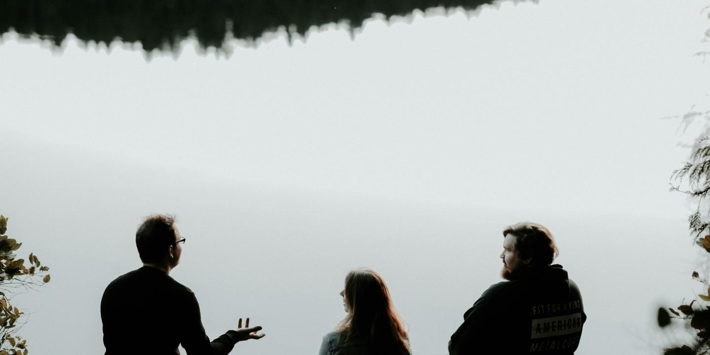Three people sitting looking out over viewpoint are silhouetted against the sky. 