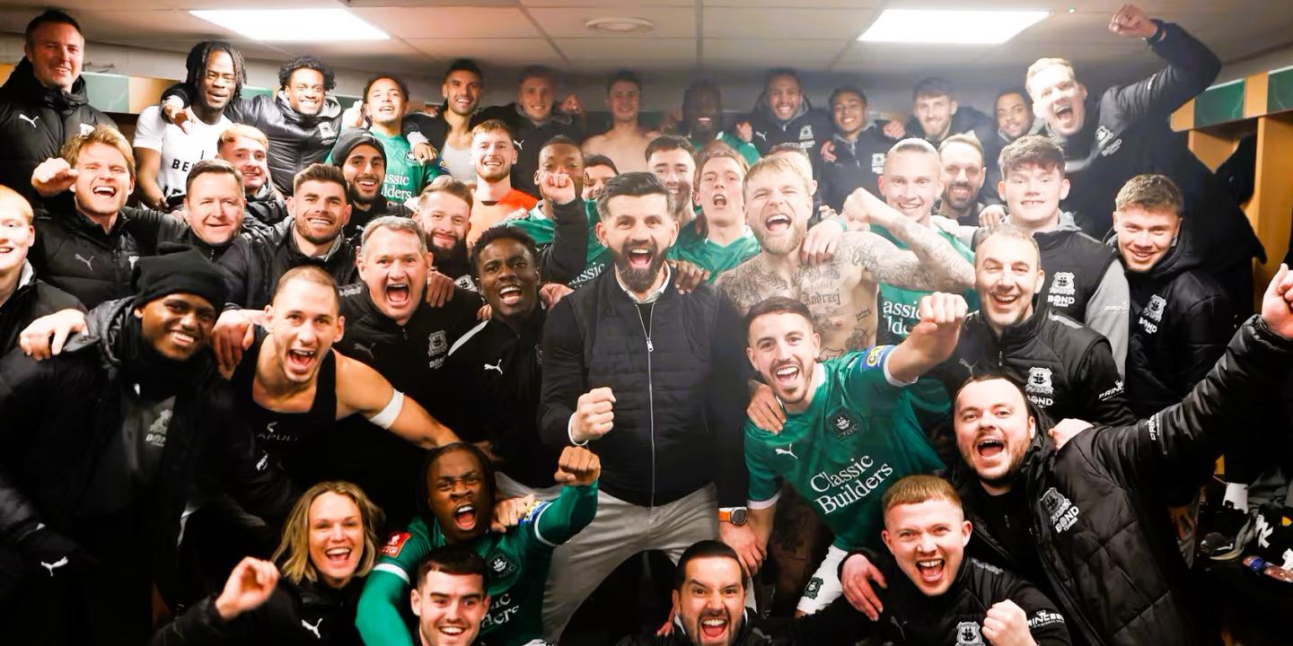 in a dressing room, celebrating footballer crowd together for a photograph.