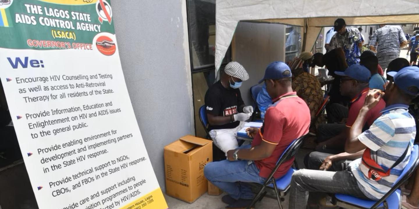 Patient wait in a street clinic beside a sign.