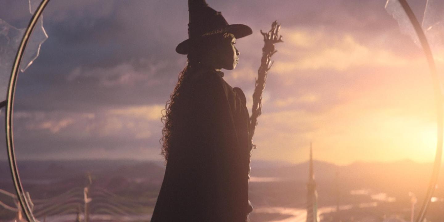 In a still from Wicked, the witch stands and looks to the sunset.