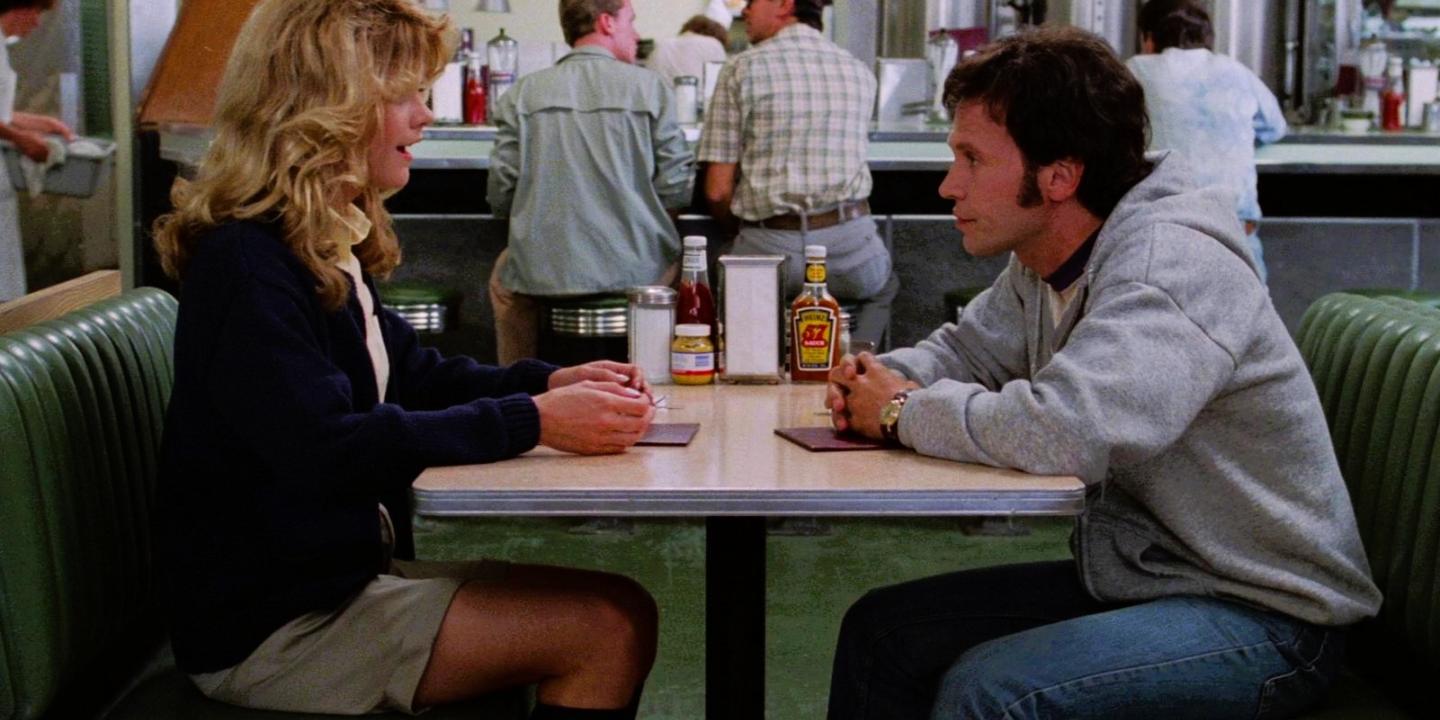 A couple sit at a table in a diner talking intensely.