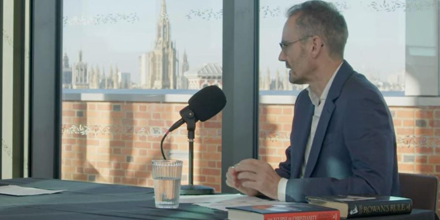 A podcast guest sits at a table in front of a mic. 