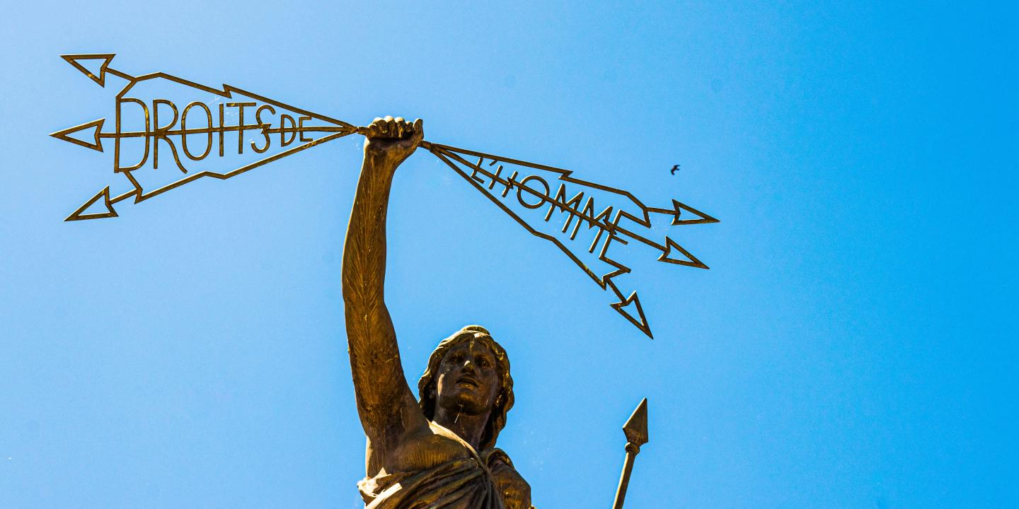 A statue of a woman holding a spear in one hand a lightening bolt in the others that reads: 'Droits de l'homme'.