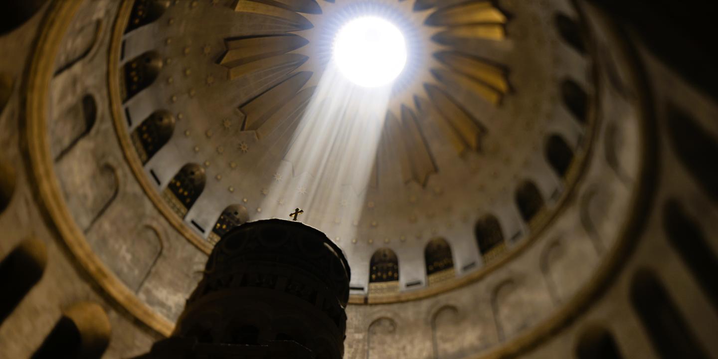 A shaft of light from an opening in a dome lights a cross on a pedestal.