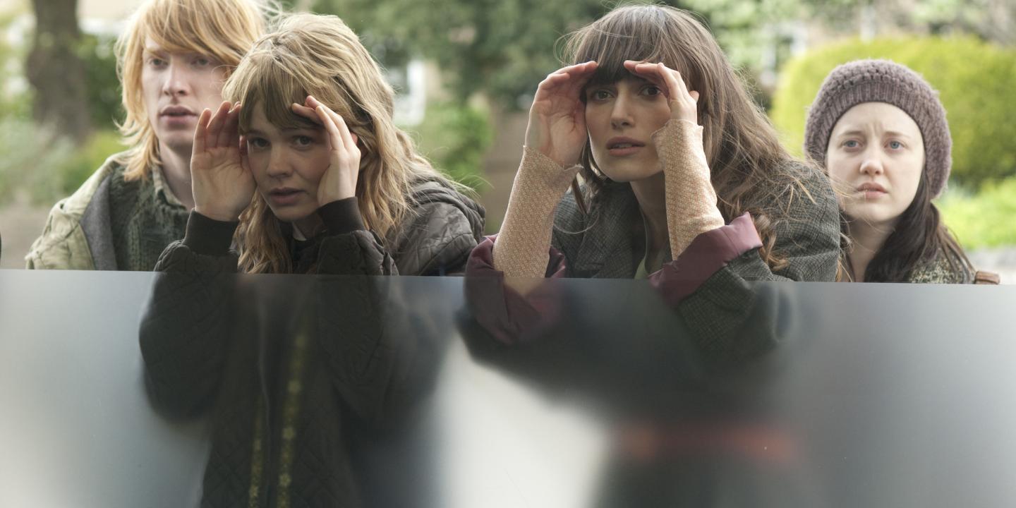 Four young people peer through a window.