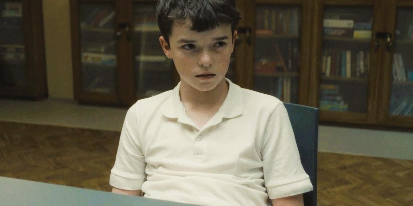A worried looking adolescent boy slumped in a chair looks up.