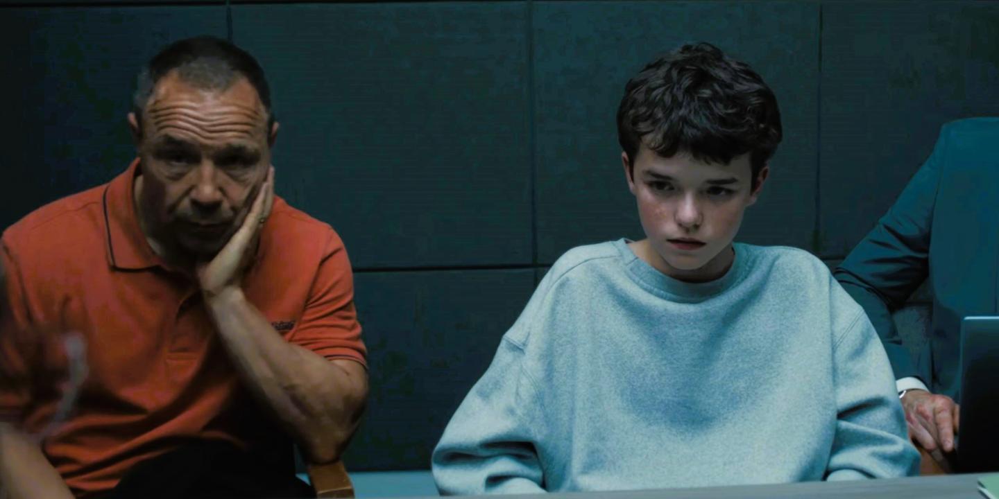 An unhappy father sits next to a scared son in a police interview room.