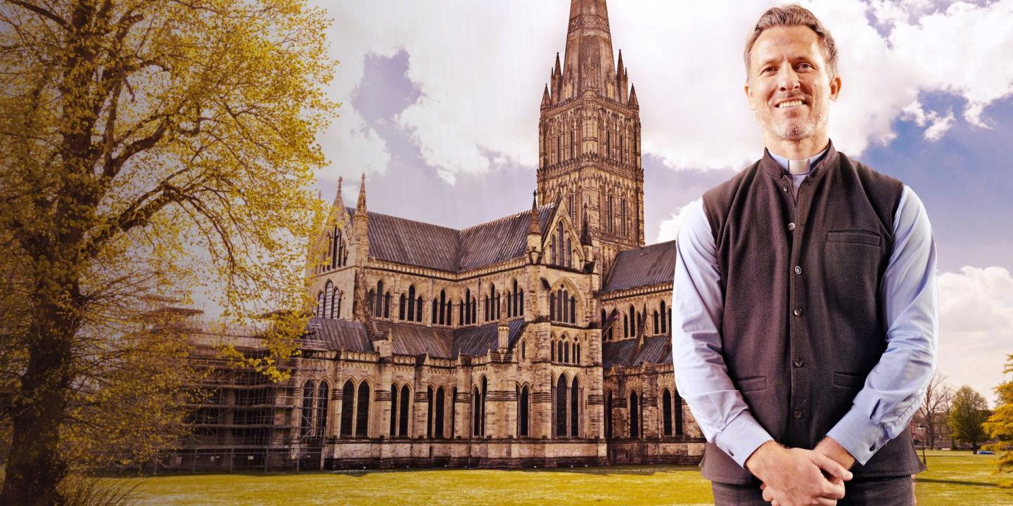 A vicar stands arms in front of himself, behind him is a cathedral