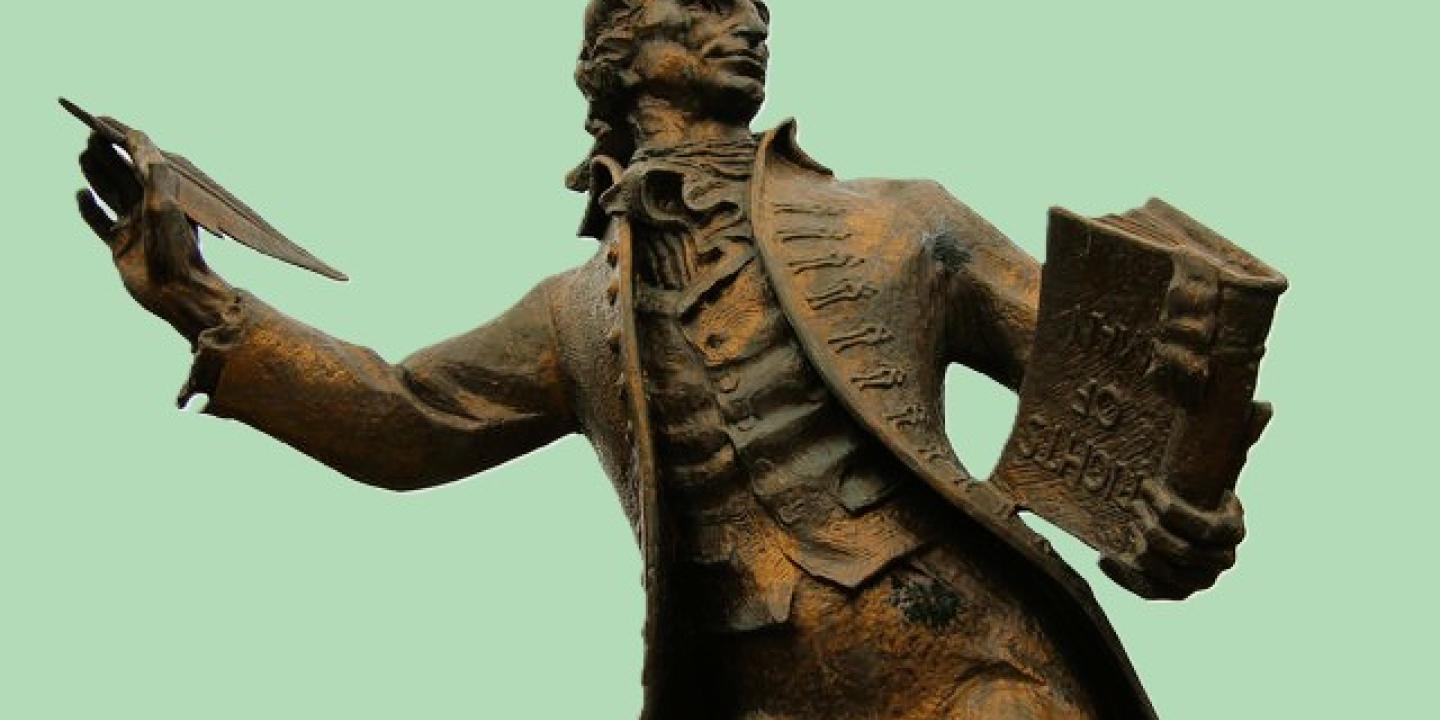 A statue of a 18th century man holding a pen and a book.