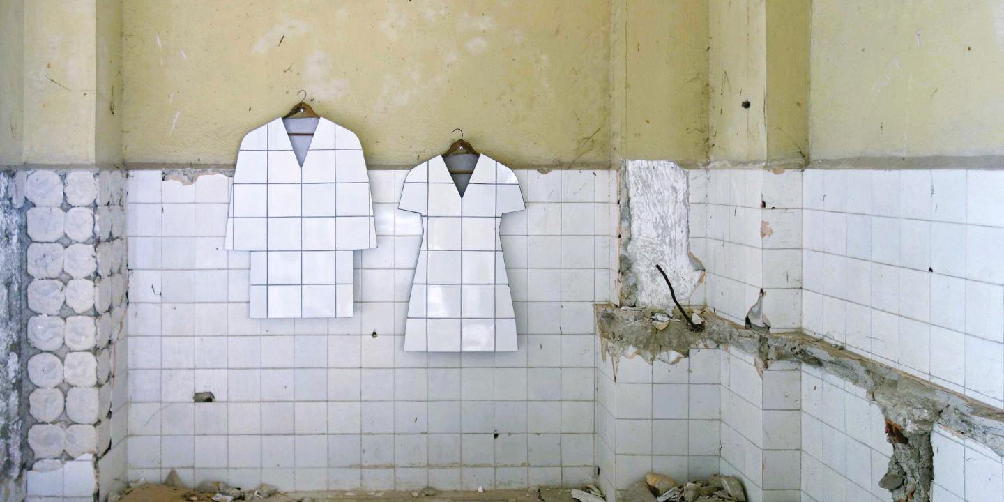 In a bombed-out tiled room, two art works hang in the shape of a tiled jacket and shape